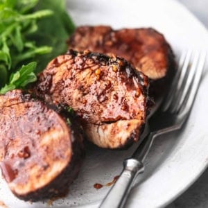 up close sliced pork tenderloin on white plate with greens and fork