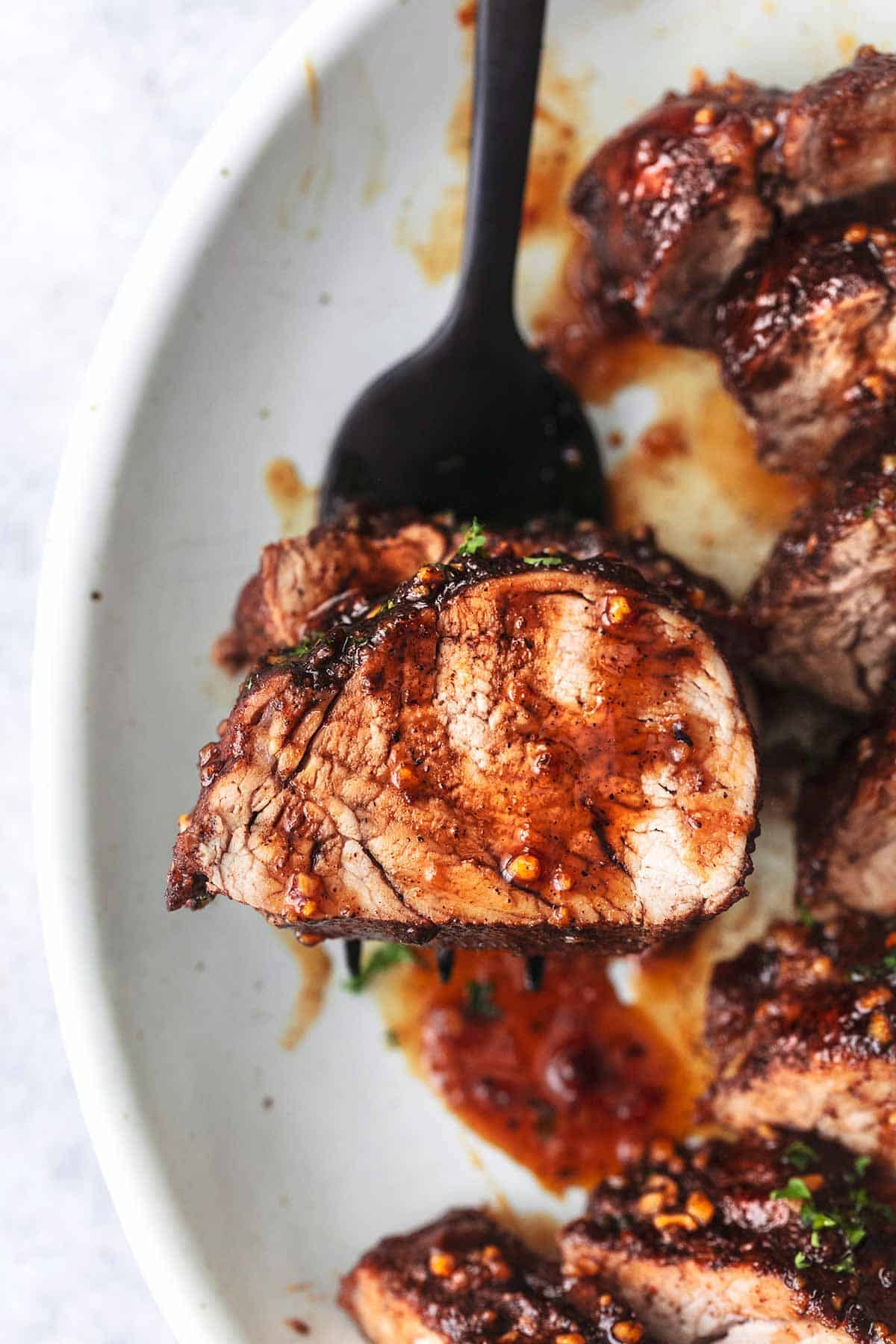 close up top view of a piece of island glazed pork tenderloin on a fork on a plate.