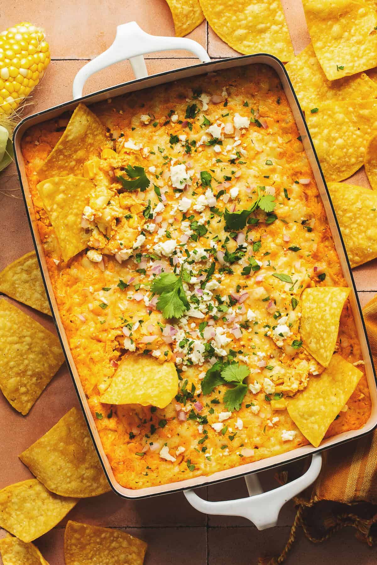 Overhead view of cheesy hot mexican street corn dip in casserole dish surrounded by tortilla chips