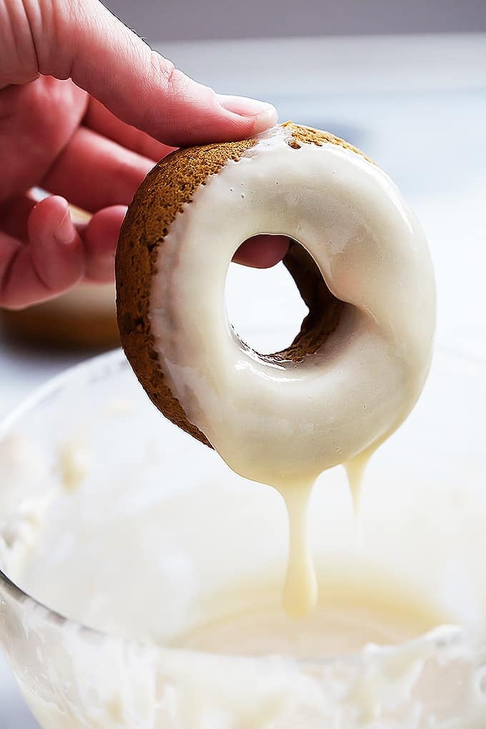 a hand picking up a baked pumpkin donut just dipped in maple glaze.