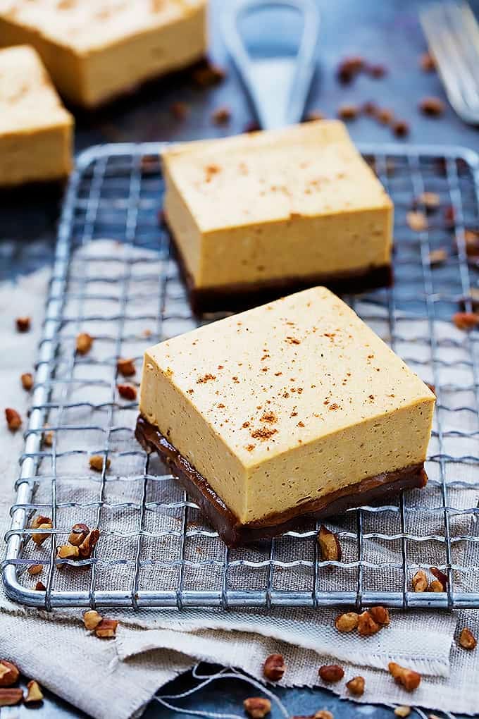 pumpkin cheesecake bars with gingersnap crust on a cooling rack with more bars on the side.