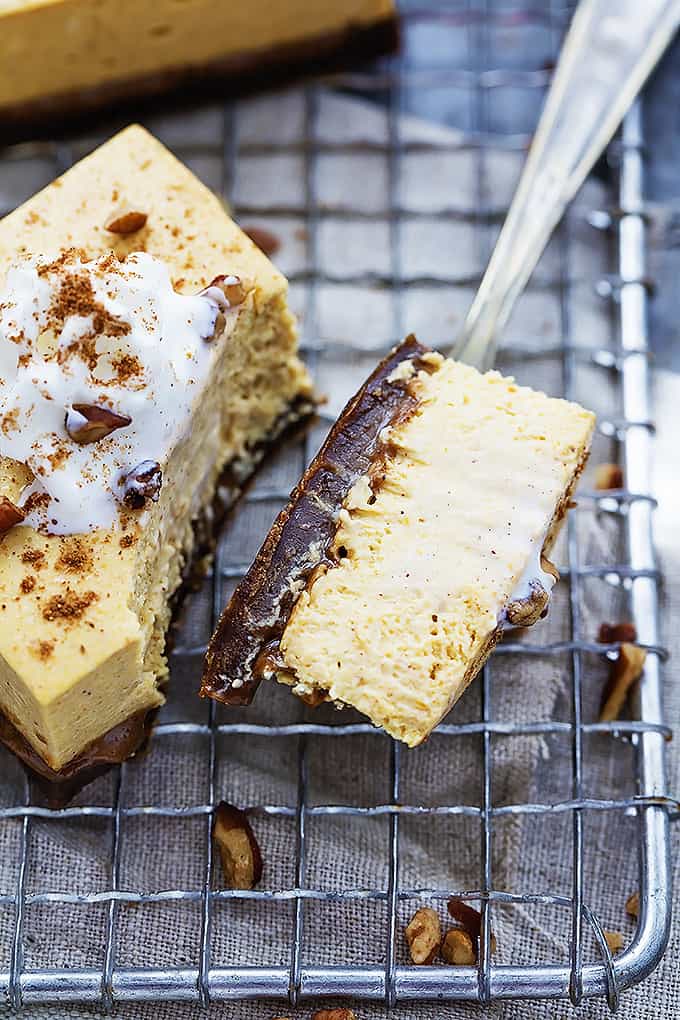 close up of a pumpkin cheesecake bar with gingersnap crust on a cooling rack with a bite missing from it sitting on top of a fork on the side.