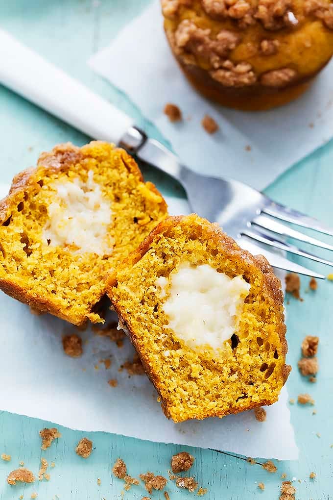a pumpkin cream cheese streusel muffin cut in half and laid on it's side with a fork and another muffin on the side.
