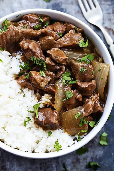 close up top view of slow cooker beef on rice in a bow with a fork on the side.