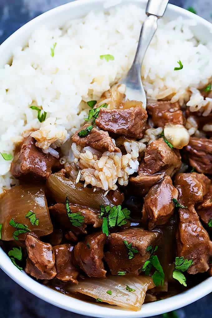 close up top view of slow cooker beef on rice in a bowl with a fork with a bite on top.