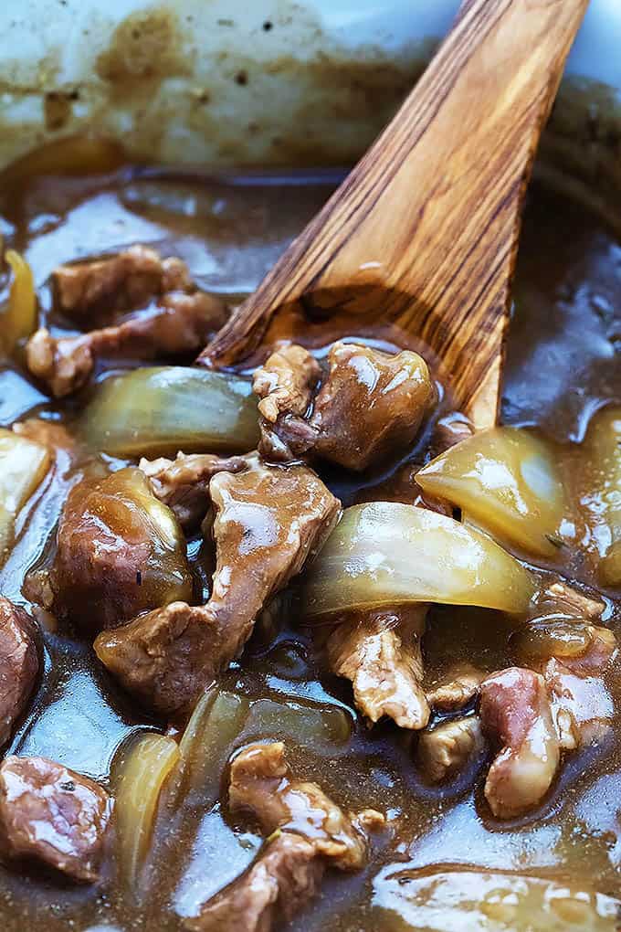 close up of slow cooker beef with a wooden serving spoon in a slow cooker.