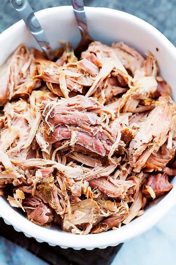 close up top view of slow cooker kalua pork with serving spoons in a bowl.