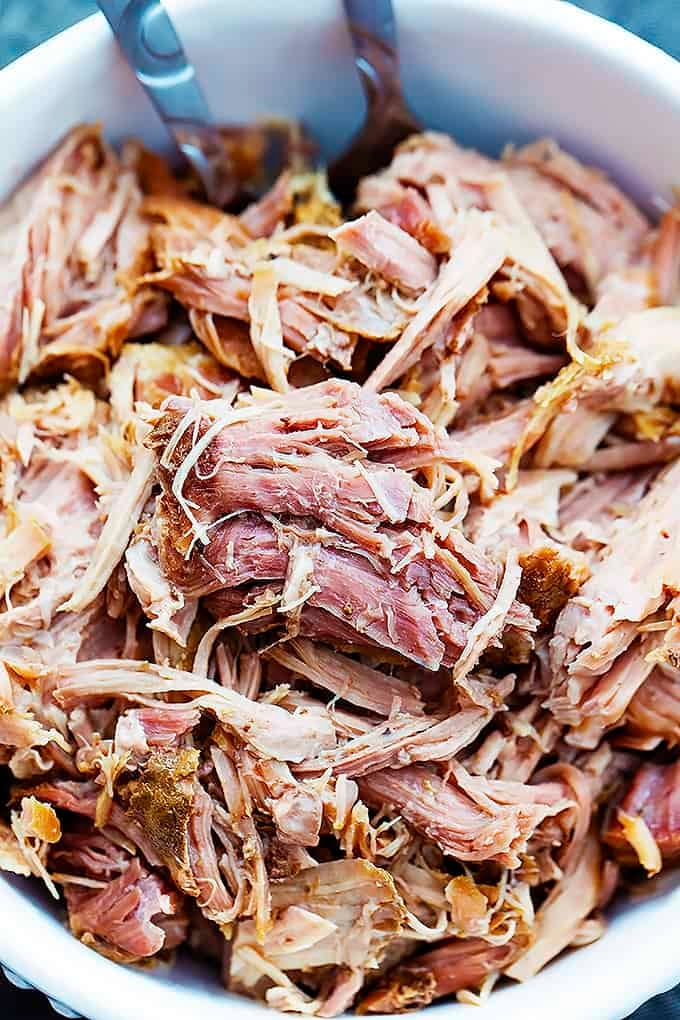 close up top view of slow cooker kalua pork with serving spoons in a bowl.