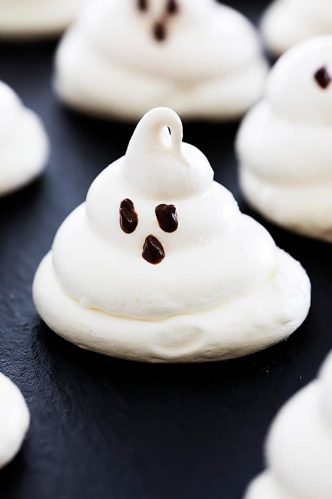 close up of an almond meringue ghost cookie with more cookies around it.