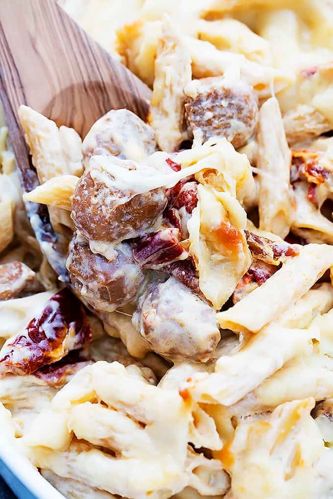 close up of baked cheesy sausage penne and a wooden serving spoon.