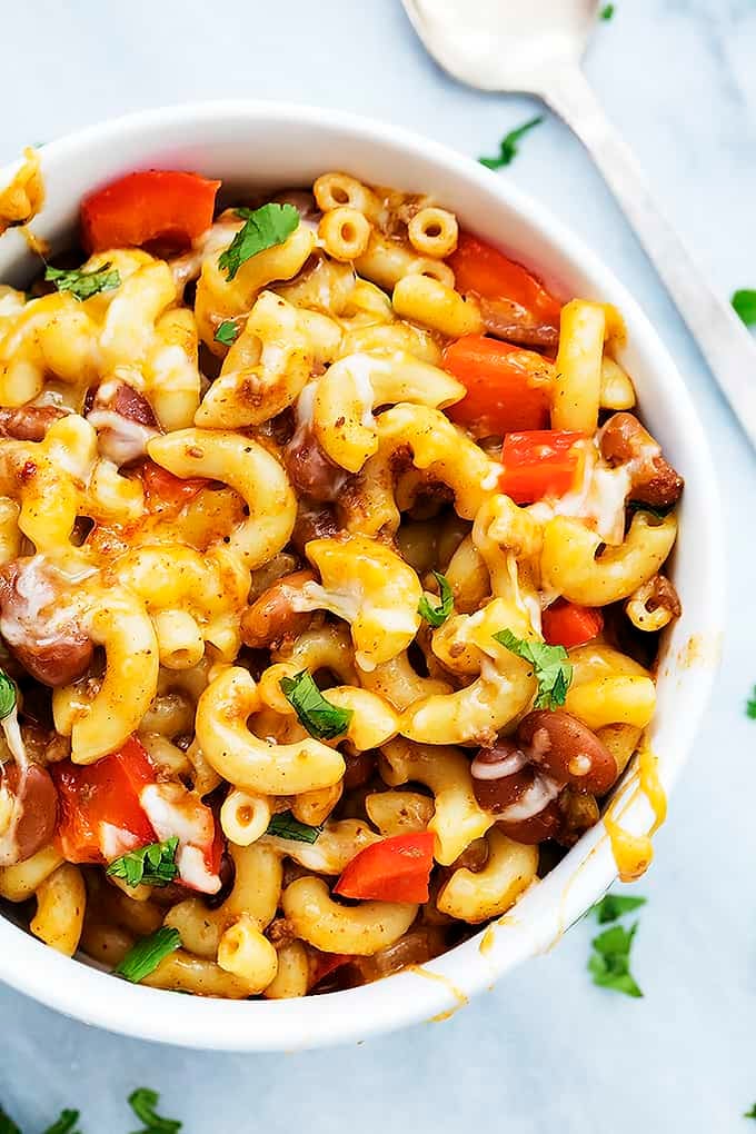 top close up view of cheesy chili mac in a bowl with a spoon on the side.