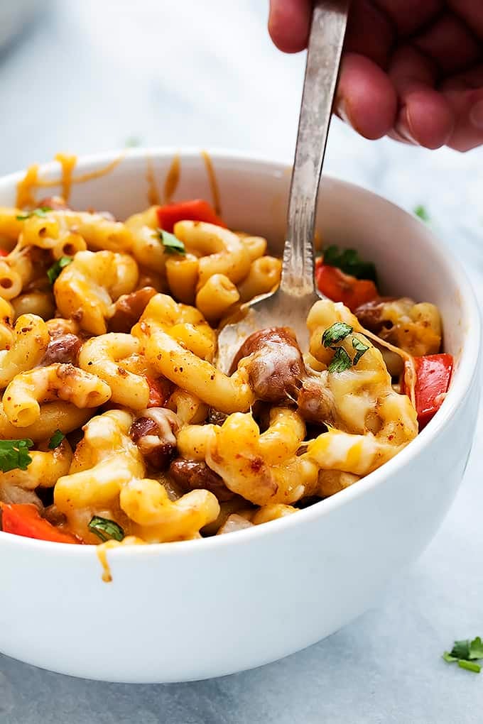 a hand holding a spoon in a bowl of cheesy chili mac.