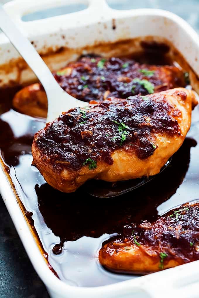 a spatula holding up a piece of slow cooker cranberry chicken above a serving tray of more chicken.