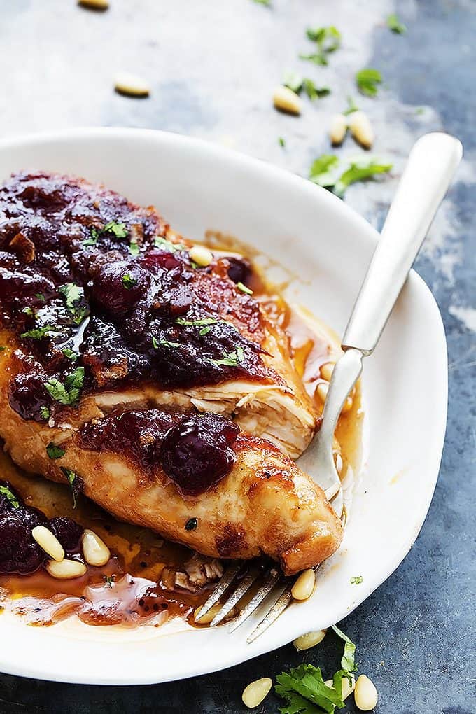 slow cooker cranberry chicken with a fork underneath the chicken on a plate.