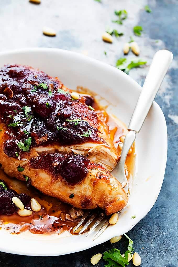 slow cooker cranberry chicken with a fork underneath the chicken on a plate.