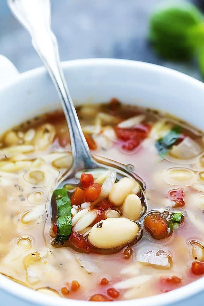 close up of a spoon of Italian white bean & orzo soup sitting on top of more soup in a bowl.