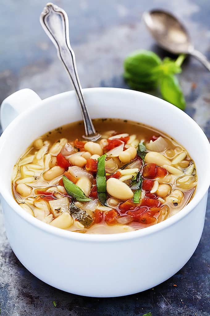 Italian white bean & orzo soup with a spoon in a bowl with another spoon on the side.
