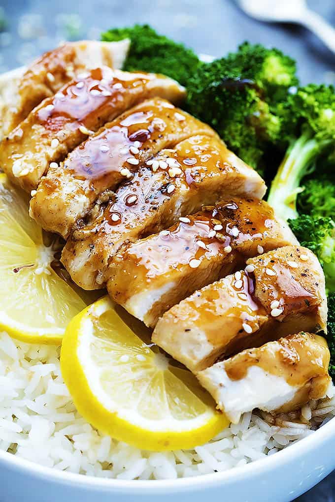close up of lemon teriyaki chicken with lemon slices and broccoli on top of rice in a bowl.