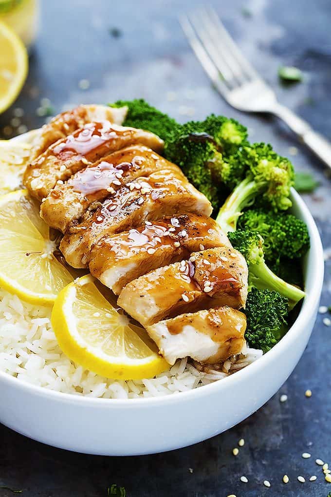 lemon teriyaki chicken with lemon slice and broccoli on rice in a bowl with a fork and more lemon slices in the background.