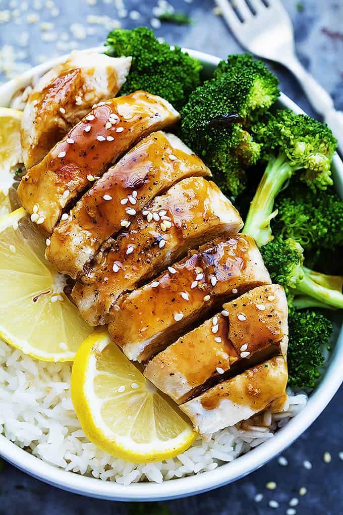 close up top view of lemon teriyaki chicken, lemon slices, and broccoli on rice in a bowl with a fork on the side.