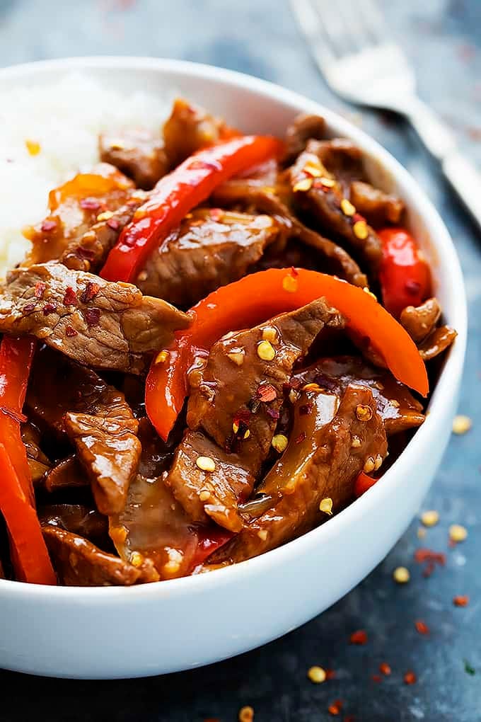 close up of sriracha orange beef with rice in a bowl with a fork on the side.