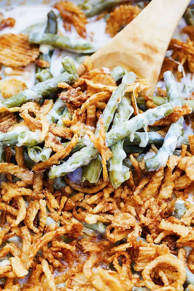 close up of slow cooker green bean casserole with a wooden serving spoon.