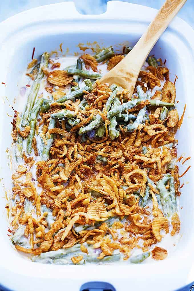 slow cooker green bean casserole with a wooden serving spoon in a serving dish.