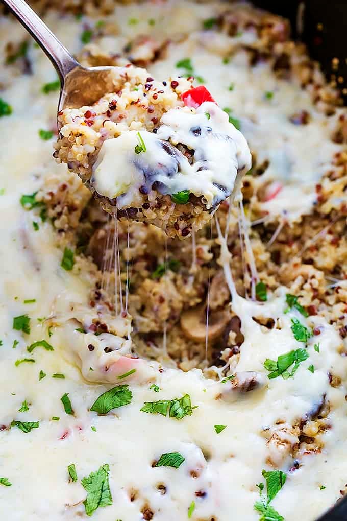 close up of a spoon lifting a spoonful of slow cooker cheesy mushroom quinoa from a slow cooker.