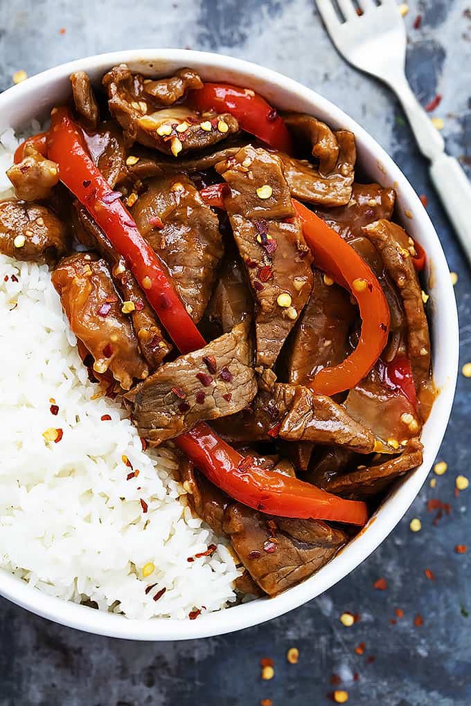 close up top view of sriracha orange beef with rice in a bowl with a fork on the side.