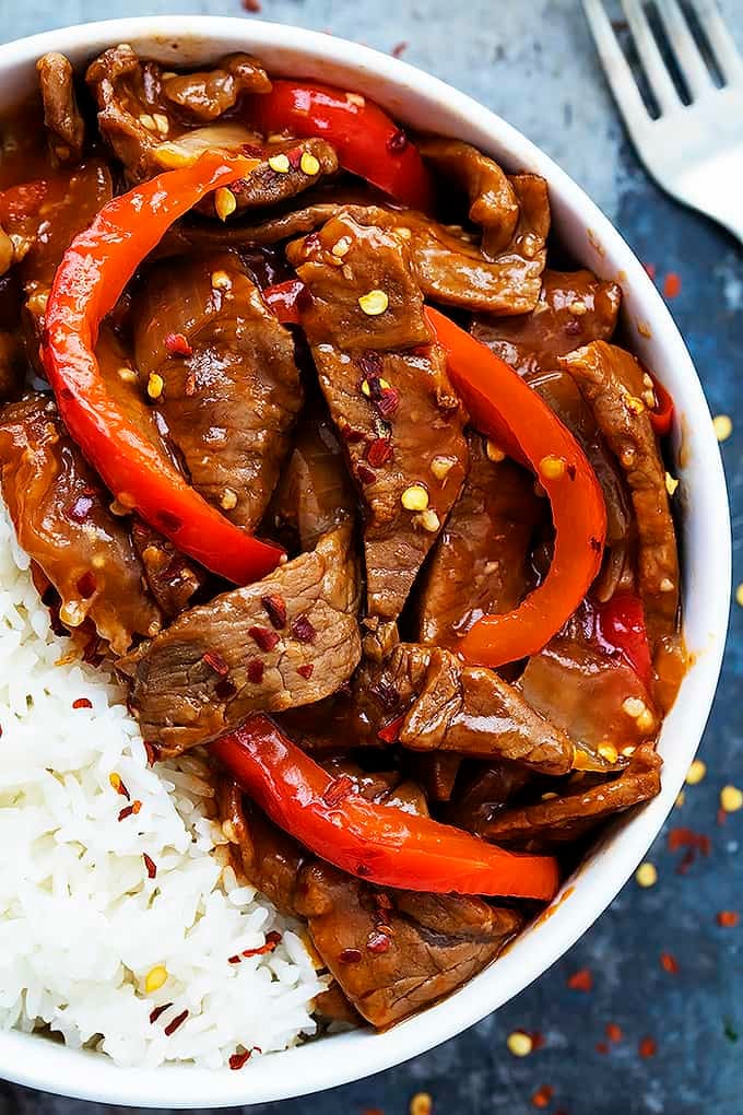 close up top view of sriracha orange beef with rice in a bowl with a fork on the side.