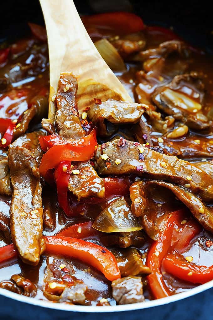 close up of sriracha orange beef with a wooden serving spoon in a cooking pot.