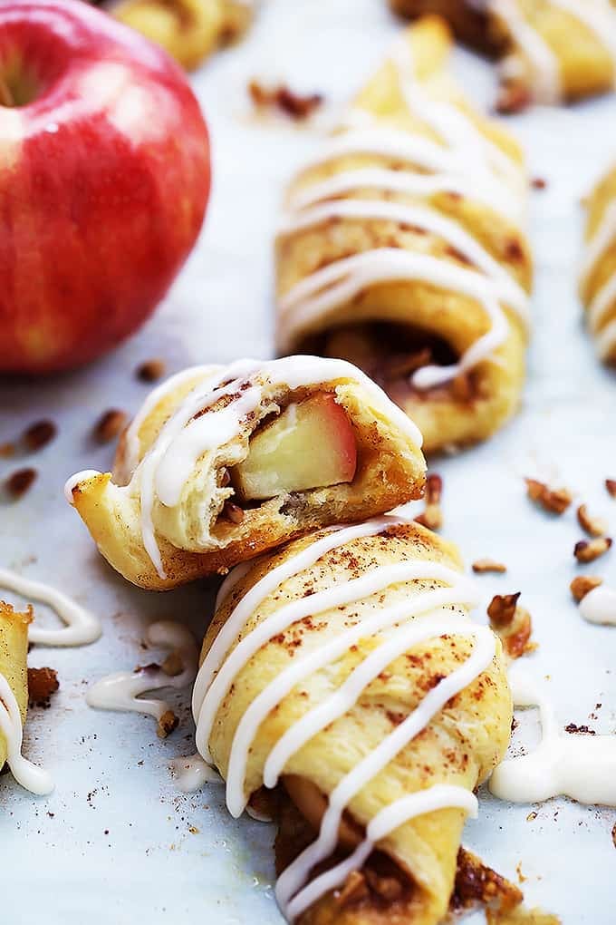a apple pie roll up leaning on another roll up with an apple and more roll ups on the side. 