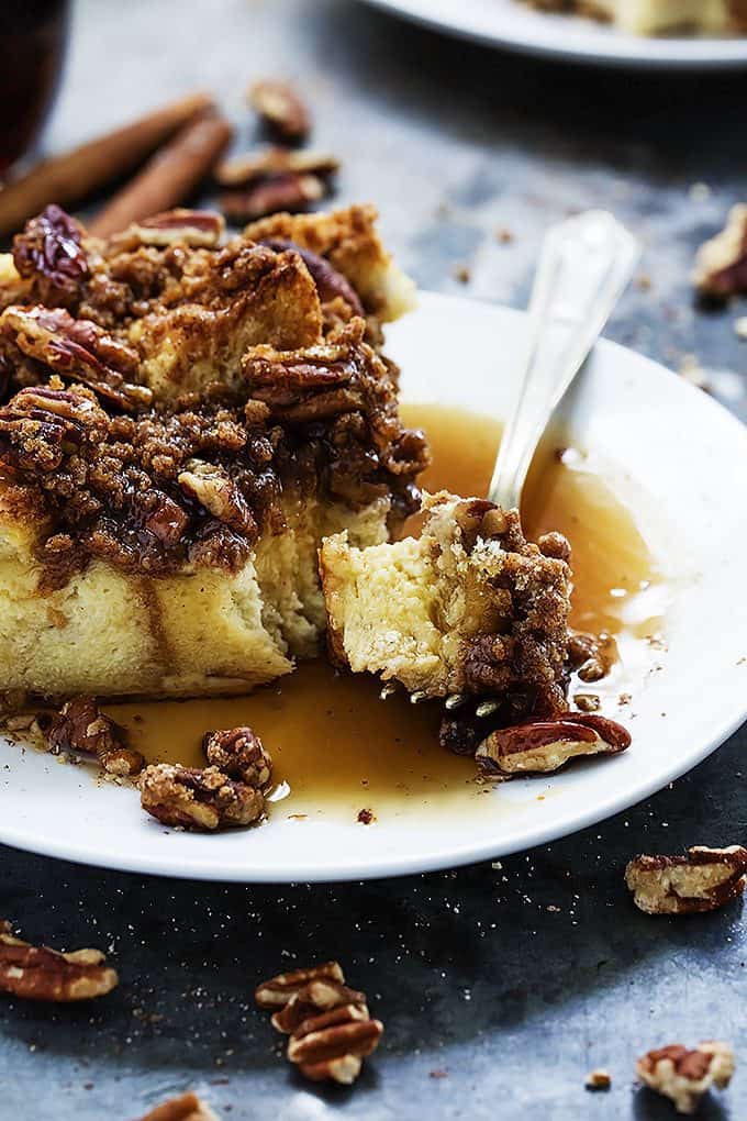 a piece of overnight cinnamon pecan French toast casserole with a bite missing with the bite on a fork on the side all on a plate.