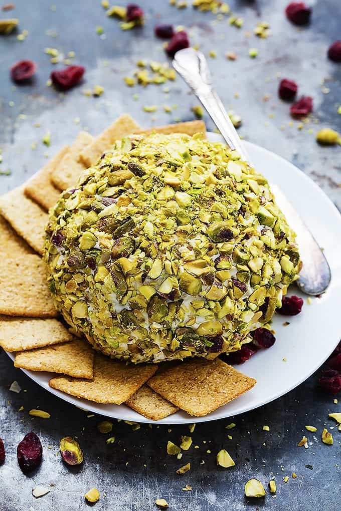 cranberry pistachio cheeseball with crackers and a knife on a plate.