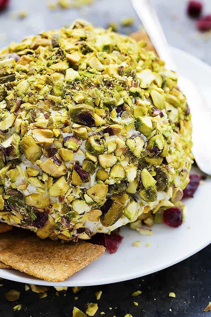 cranberry pistachio cheeseball with crackers and a knife on a plate.