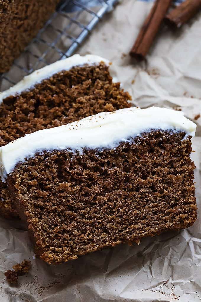 close up of gingerbread loaf with cream cheese frosting laying on top of each other with cinnamon sticks on the side.