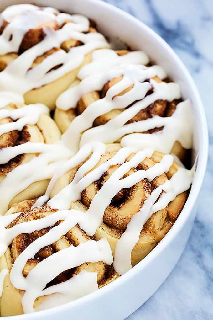 close up of mashed potato cinnamon rolls topped with icing in a round dish.