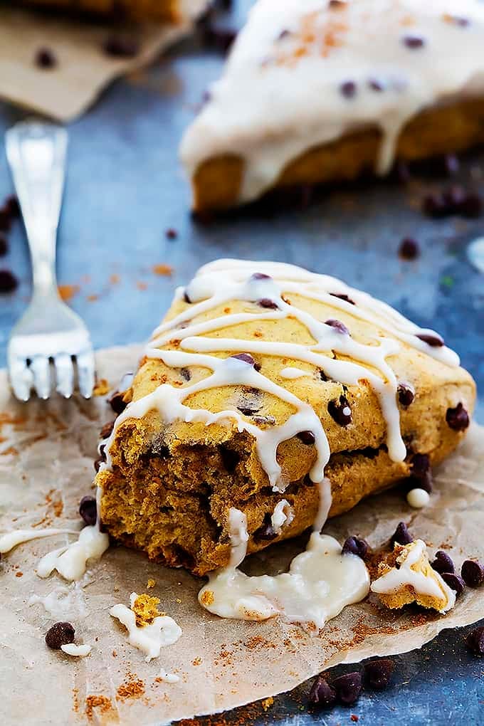 a pumpkin chocolate chip scone drizzled with cream cheese frosting with a bite missing and a fork on the side.