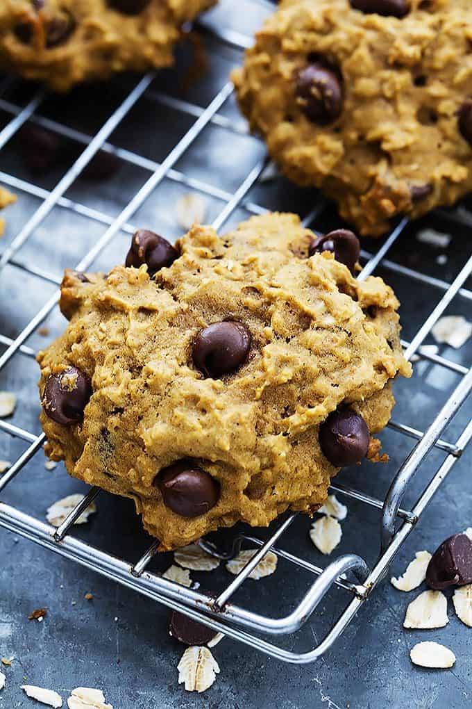 close up of a pumpkin oat chocolate chip cookie with more cookies on the side all on a cooling rack.