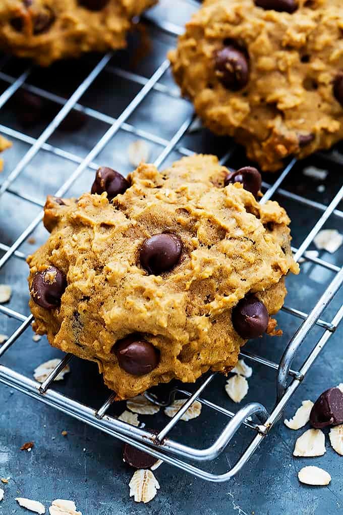 close up of a pumpkin oat chocolate chip cookie with more cookies on the side all on a cooling rack.