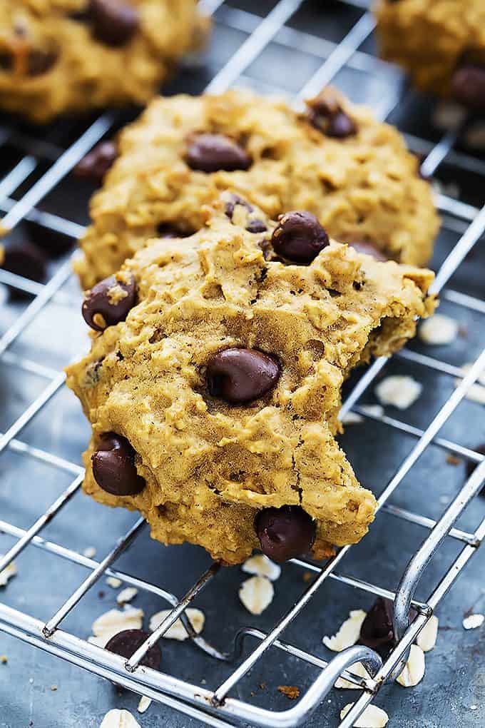 a pumpkin oat chocolate chip cookie with a bite missing leaning on top of another cookie on a cooling rack.
