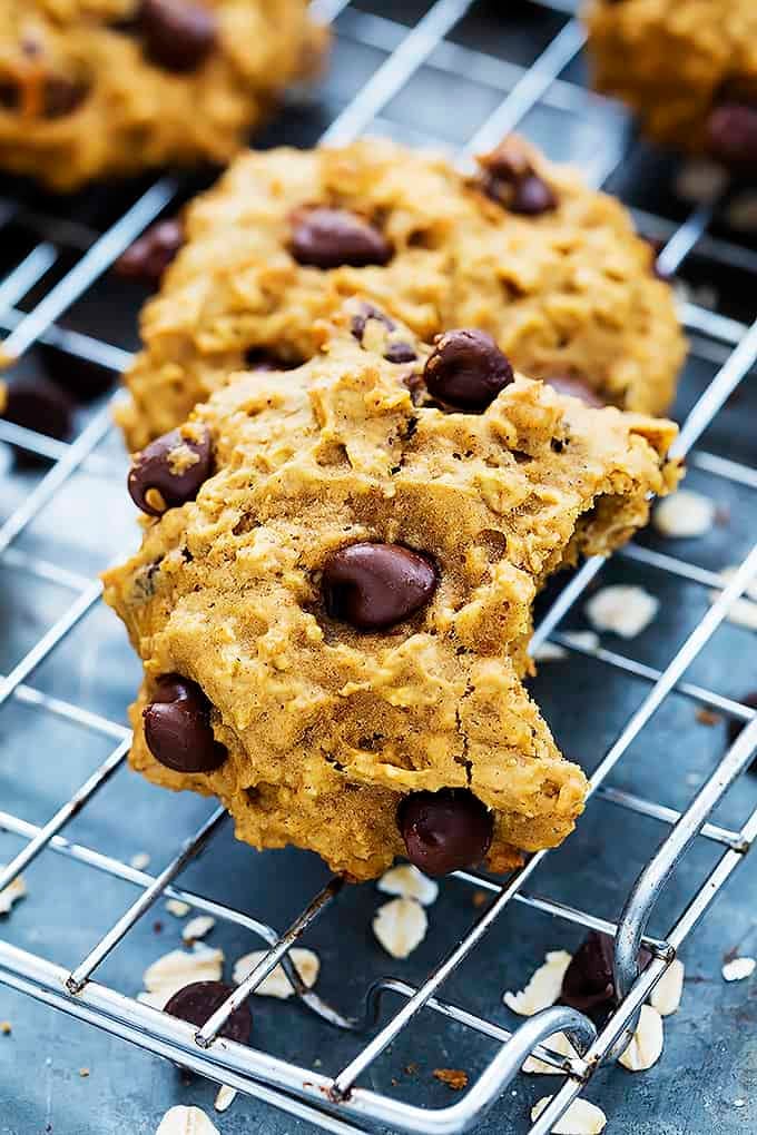 a pumpkin oat chocolate chip cookie with a bite missing leaning on top of another cookie on a cooling rack.