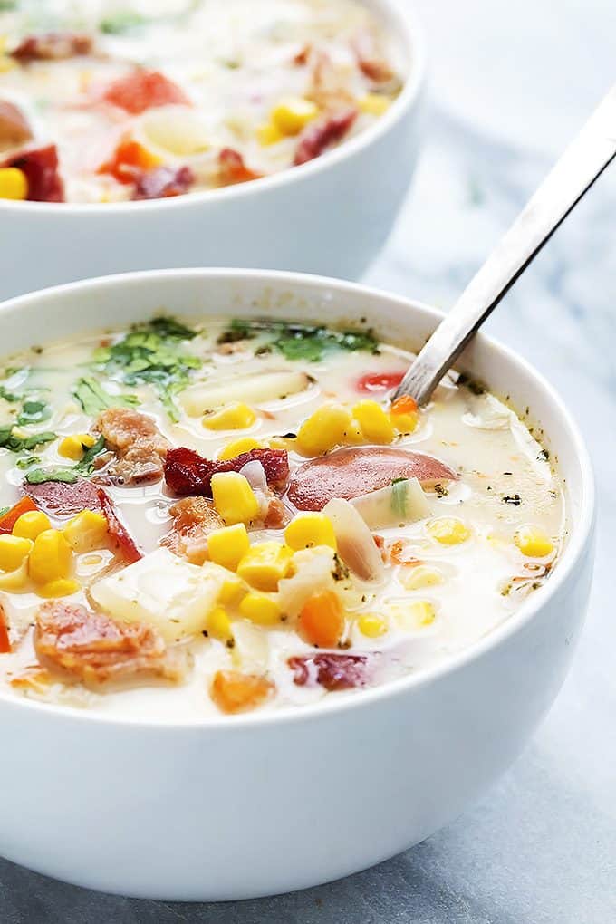 slow cooker potato bacon corn chowder with a spoon in a bowl with another bowl of chowder in the background. 