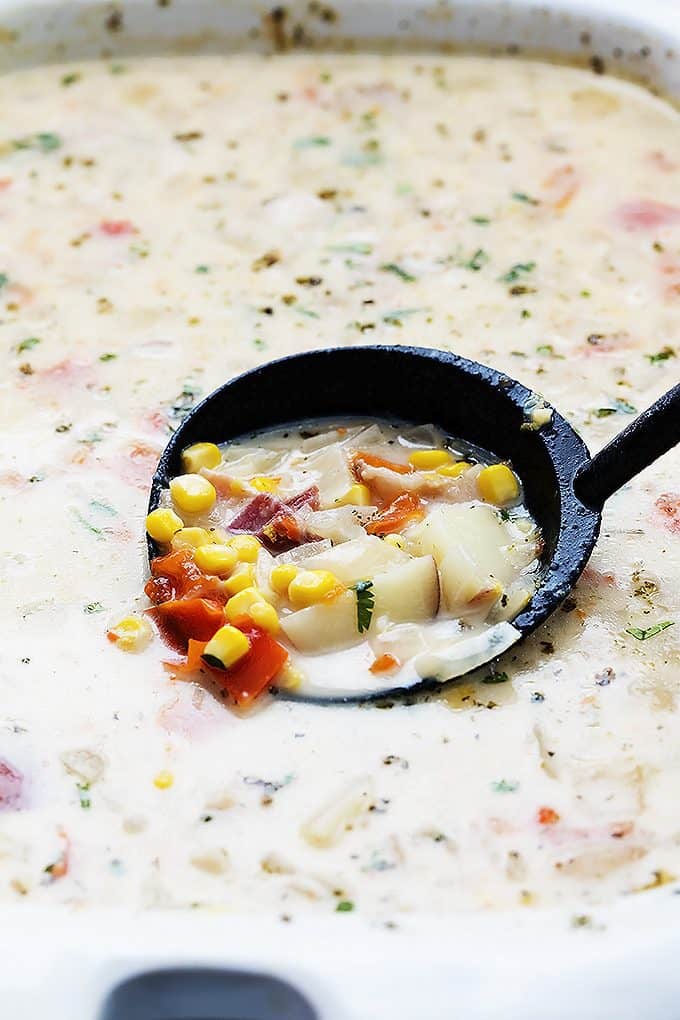 close up of a serving spoon in slow cooker potato bacon corn chowder in a serving bowl.
