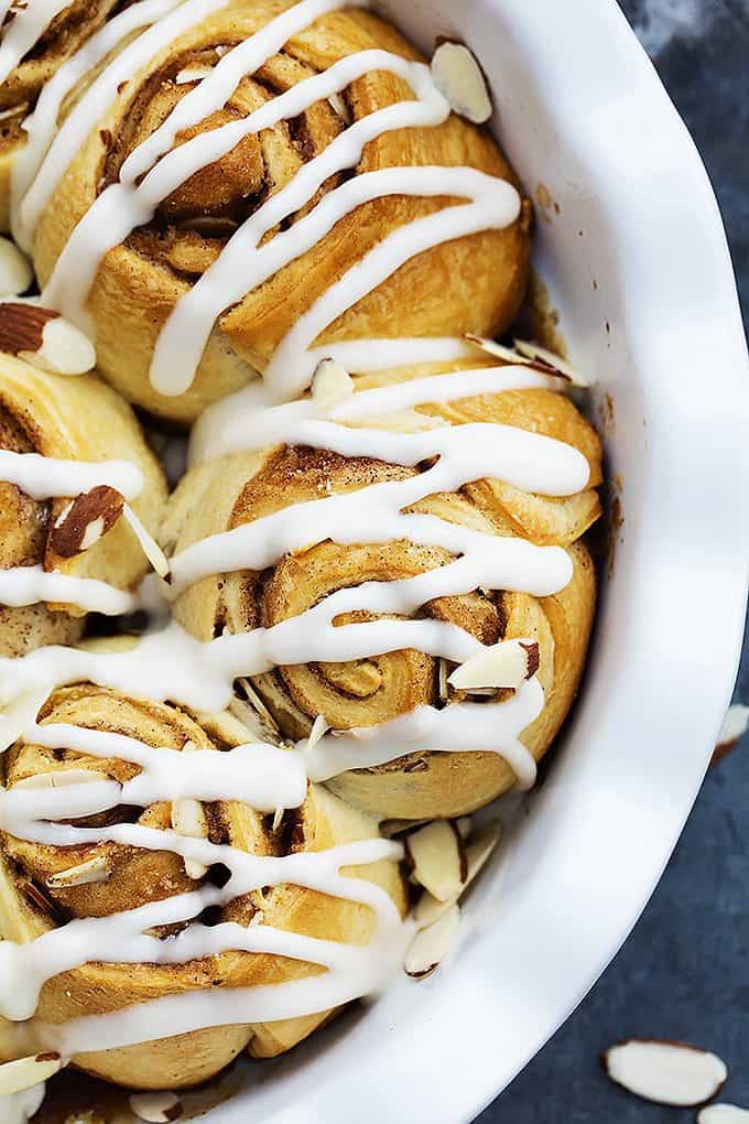 close up top view of flaky almond cinnamon buns in a round dish.