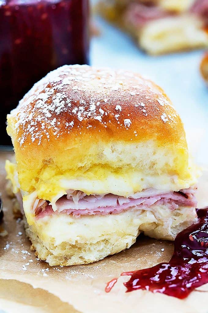 close up of a baked Monte Cristo party slider with a jar of raspberry preserves and more sliders in the background.