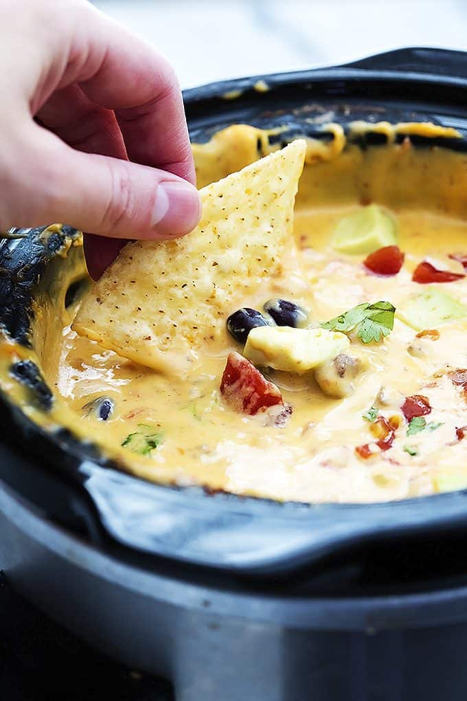 a hand dipping a chip in slow cooker taco queso dip in a slow cooker.