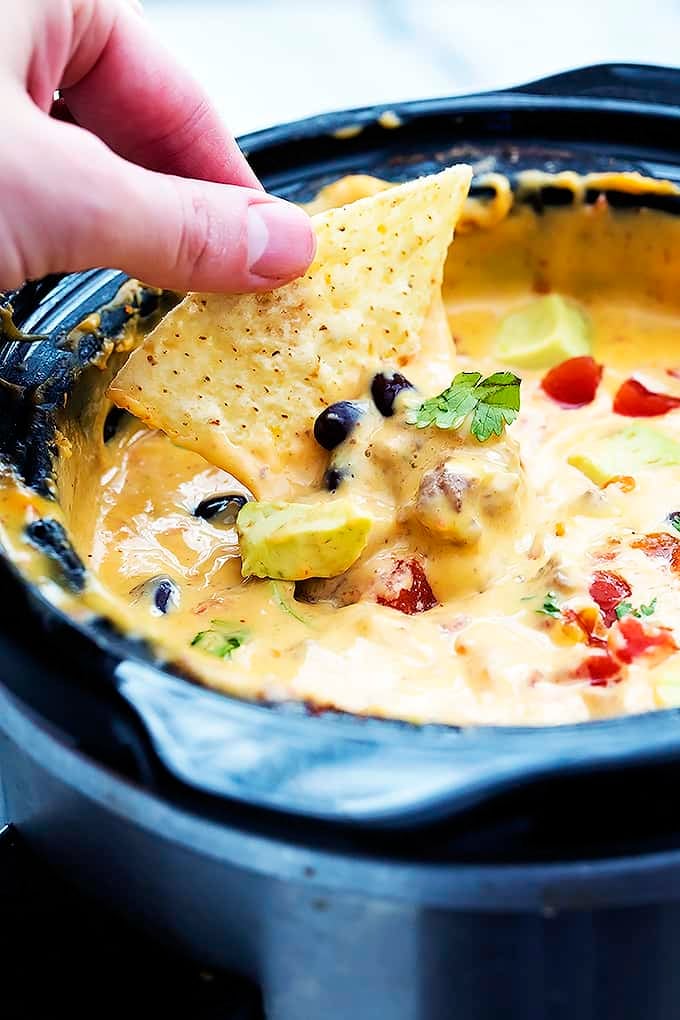 a hand dipping a chip in slow cooker taco queso dip in a slow cooker.