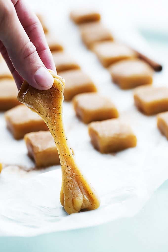 a hand pulling a vanilla cinnamon caramel off of wax paper with more caramels in the background.