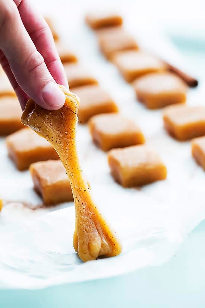 a hand pulling a vanilla cinnamon caramel off of wax paper with more caramels in the background.